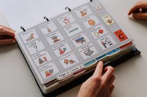 AAC_PODD Book 1 page I page PODD book on desk with multiple people's hands on desk