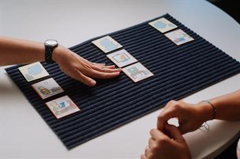 AAC_Key word speech 3 rows of picture cards on mat on desk with hand indicating middle row and others hands together on desk