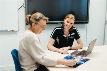Indigo-91 Female Indigo speech pathologists with older female at a desk looking at laptop and brochures